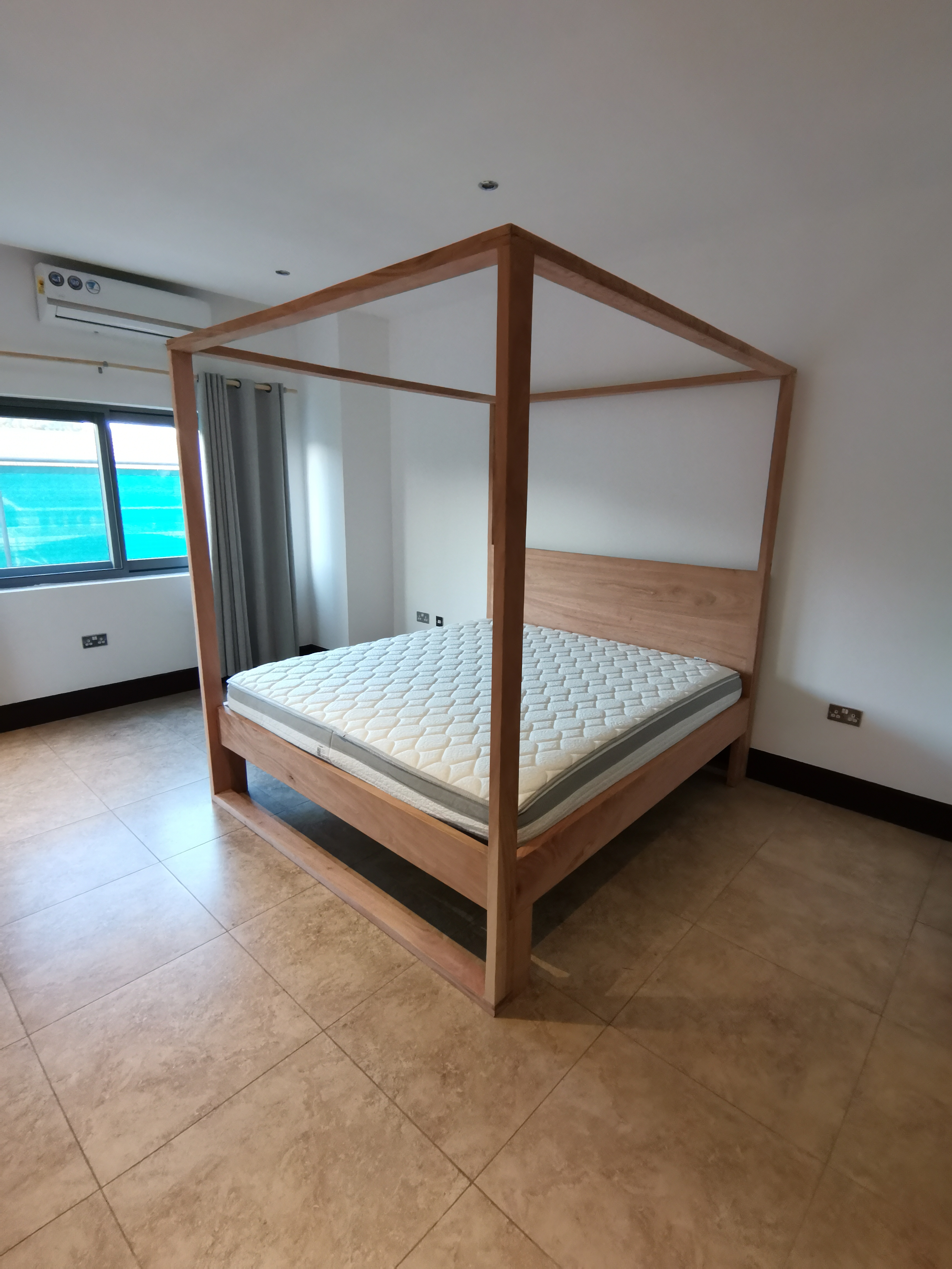 Custom solid wood four-poster bed with slatted headboard, installed at a private residence in Ridge, Accra